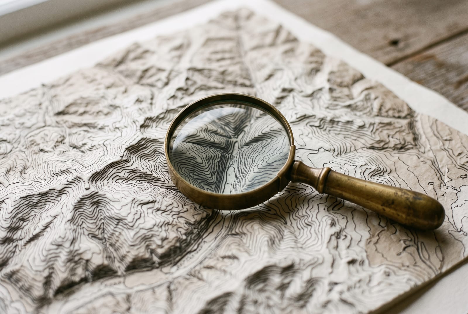 A brass magnifying glass on a relief map with contour lines